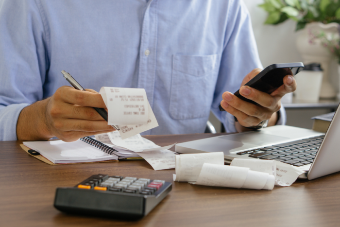 Un indépendant trie ses reçus, calculatrice et ordinateur à portée de main